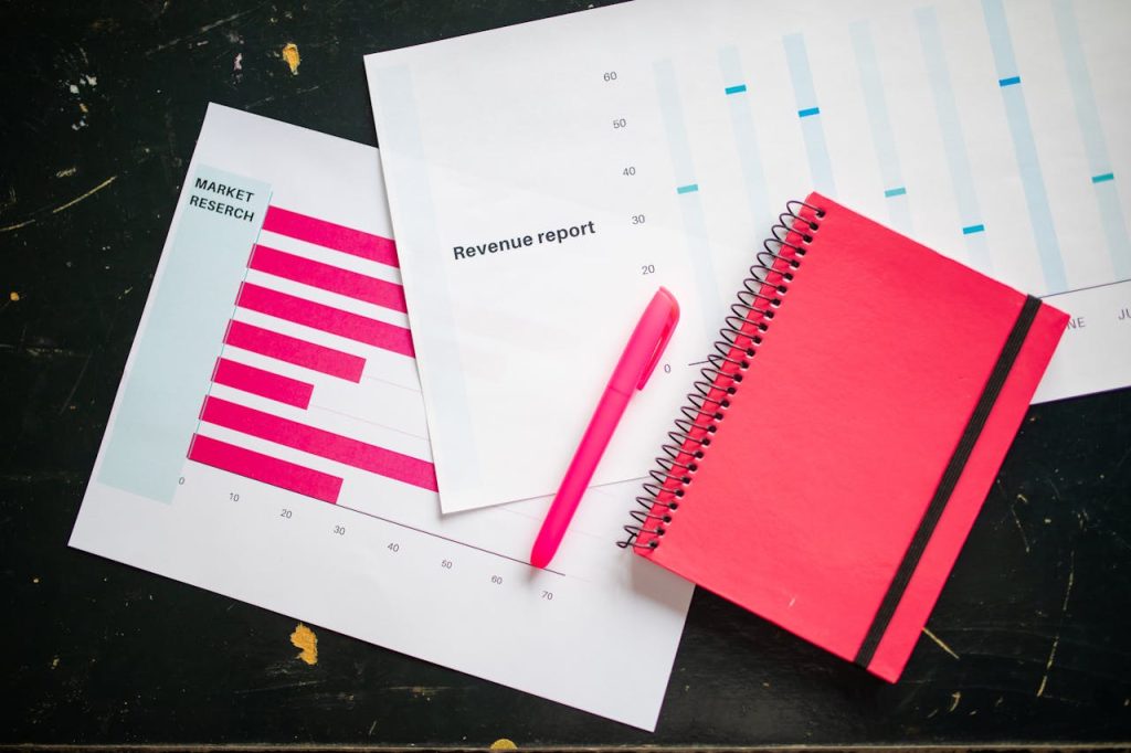 Market research and revenue report charts on a desk with a red notebook and pen, representing analysis of high-dividend stocks in 2024 for consistent income and financial stability