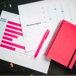 Market research and revenue report charts on a desk with a red notebook and pen, representing analysis of high-dividend stocks in 2024 for consistent income and financial stability